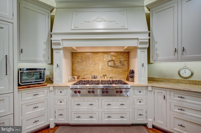 kitchen with light stone countertops, tasteful backsplash, stainless steel gas stovetop, and hardwood / wood-style flooring