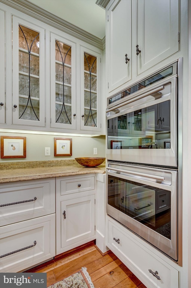 kitchen with white cabinets, light stone countertops, light wood-type flooring, and double oven