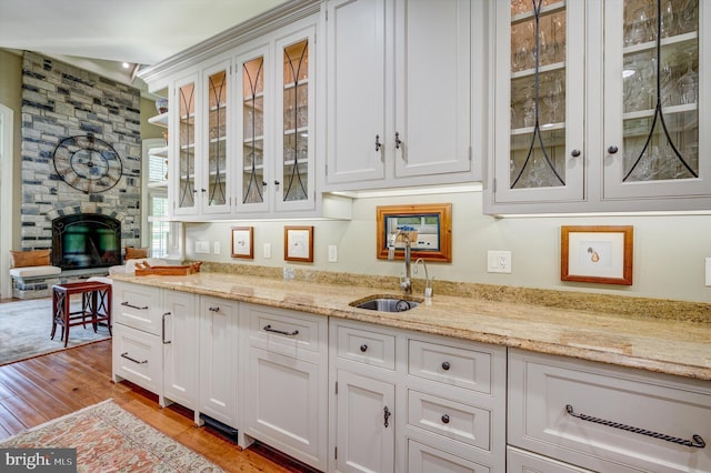 bar featuring white cabinetry, a large fireplace, sink, light stone counters, and light hardwood / wood-style flooring