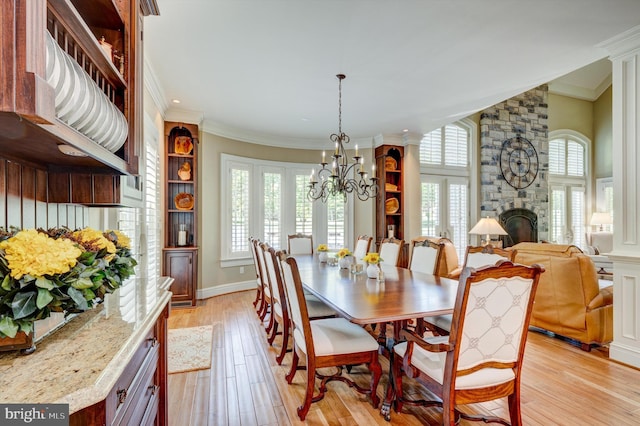 dining space featuring a fireplace, decorative columns, light hardwood / wood-style flooring, and ornamental molding