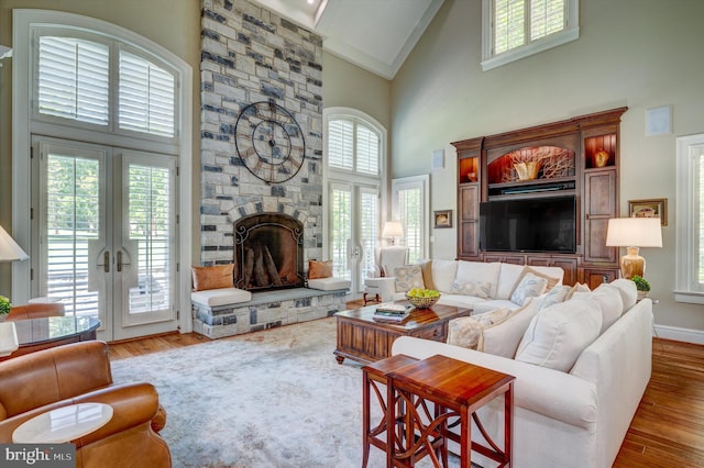 living room featuring hardwood / wood-style floors, high vaulted ceiling, french doors, and a stone fireplace