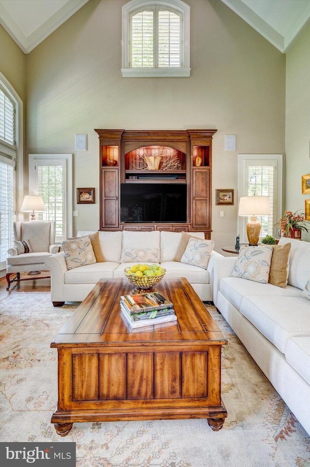 living room with a wealth of natural light, high vaulted ceiling, light wood-type flooring, and ornamental molding