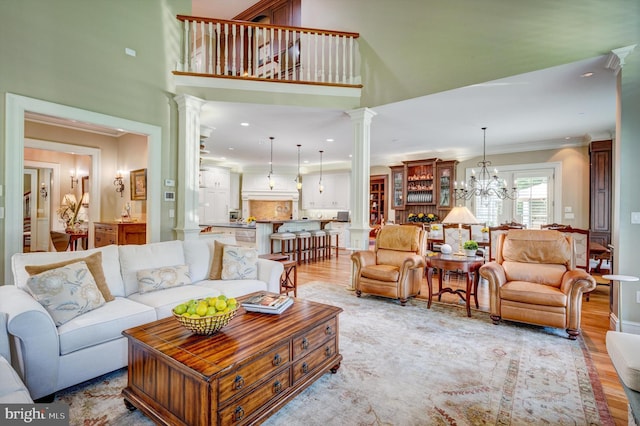 living room featuring a towering ceiling, decorative columns, ornamental molding, an inviting chandelier, and light hardwood / wood-style flooring