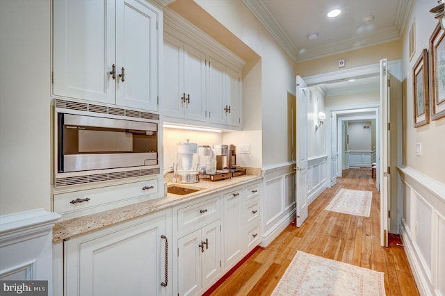 bar featuring light wood-type flooring, light stone counters, ornamental molding, white cabinets, and stainless steel microwave