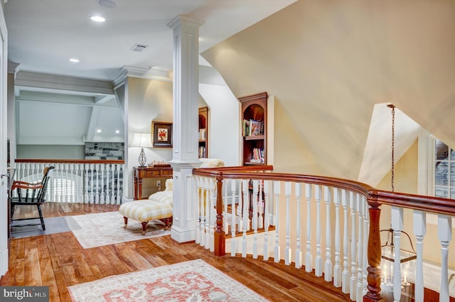 corridor with ornate columns, wood-type flooring, lofted ceiling, and ornamental molding