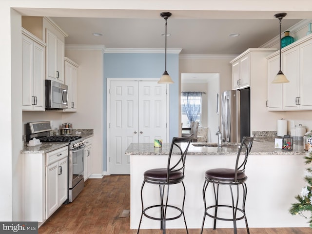 kitchen with dark wood-type flooring, light stone countertops, appliances with stainless steel finishes, decorative light fixtures, and white cabinetry