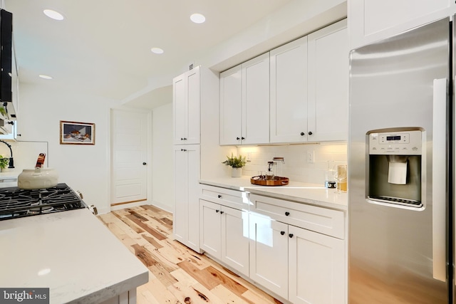 kitchen with stainless steel refrigerator with ice dispenser, light wood-type flooring, tasteful backsplash, and white cabinetry