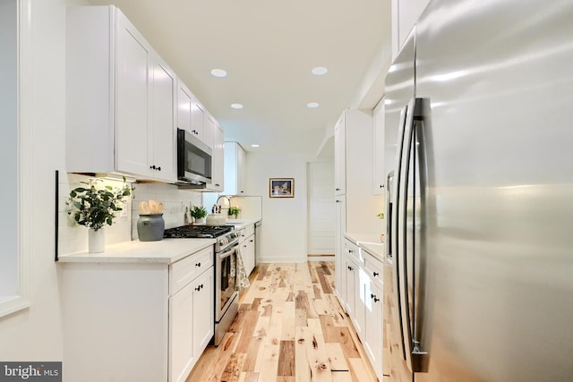 kitchen featuring sink, decorative backsplash, light wood-type flooring, white cabinetry, and stainless steel appliances