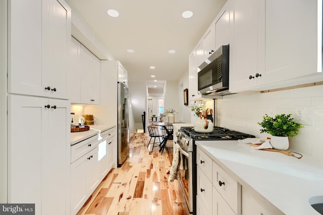 kitchen with white cabinets, tasteful backsplash, appliances with stainless steel finishes, and light hardwood / wood-style flooring