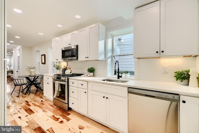 kitchen featuring white cabinets, sink, light hardwood / wood-style flooring, decorative backsplash, and appliances with stainless steel finishes