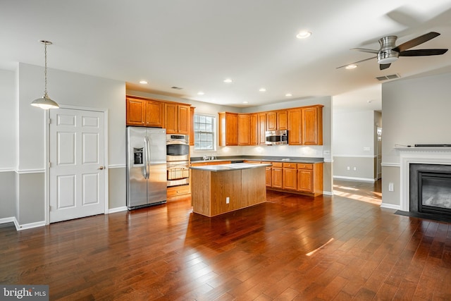 kitchen featuring dark wood-type flooring, appliances with stainless steel finishes, decorative light fixtures, and a kitchen island