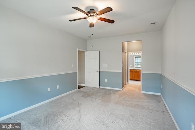 unfurnished bedroom featuring ensuite bathroom, light colored carpet, and ceiling fan