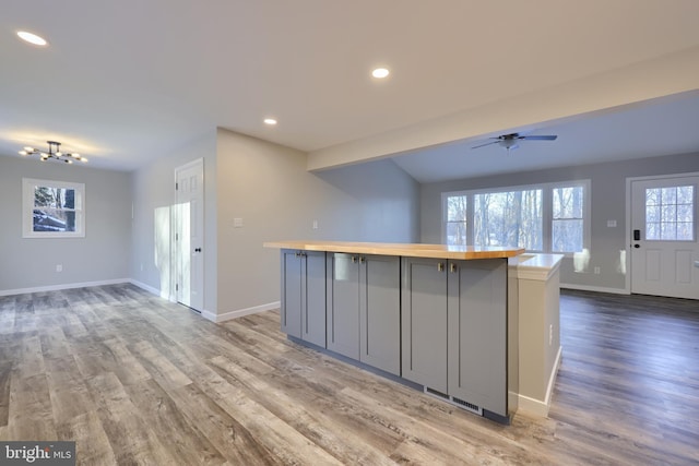 kitchen with gray cabinetry, a center island, ceiling fan with notable chandelier, and butcher block counters