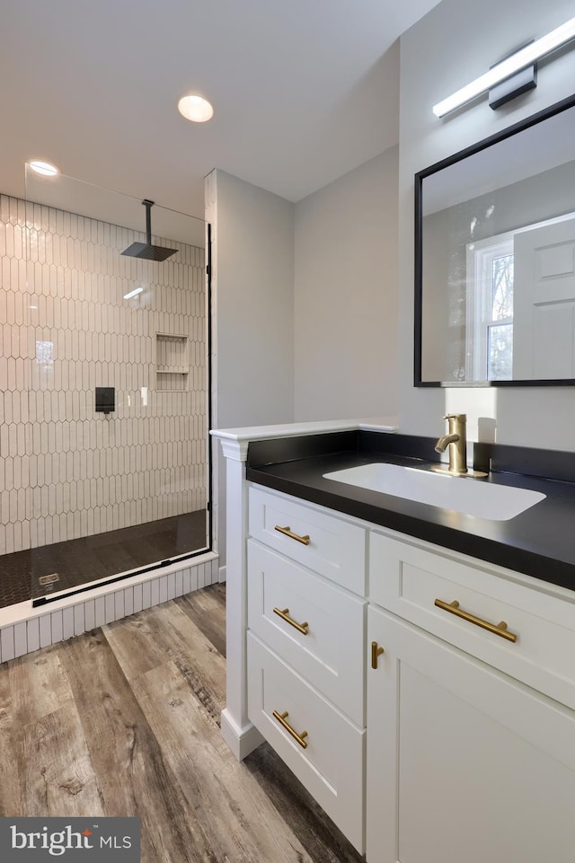 bathroom featuring a tile shower, vanity, and wood-type flooring