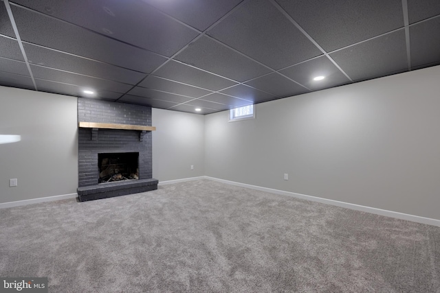 basement featuring carpet flooring, a paneled ceiling, and a brick fireplace