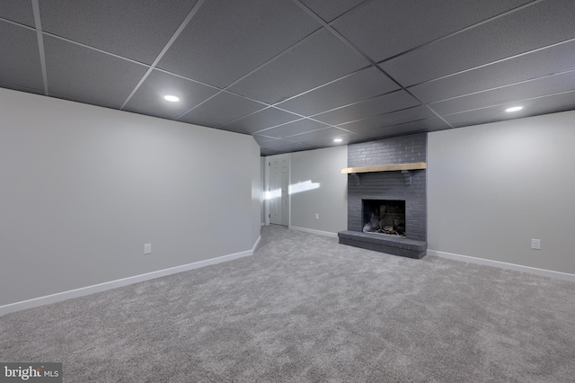 basement featuring a drop ceiling, carpet floors, and a brick fireplace