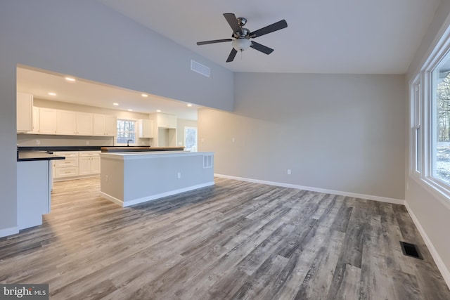 kitchen with ceiling fan, a center island, lofted ceiling, white cabinets, and light wood-type flooring