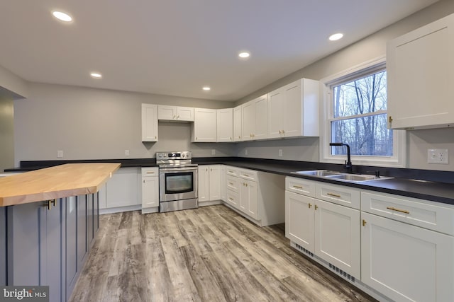 kitchen with butcher block counters, stainless steel range with electric cooktop, sink, light hardwood / wood-style floors, and white cabinetry