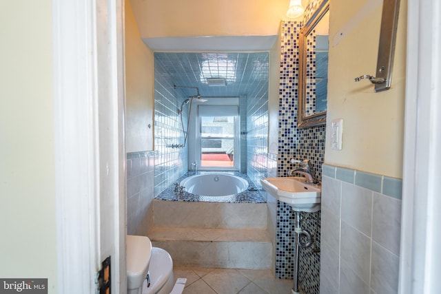 bathroom with tile patterned floors, toilet, sink, tile walls, and a relaxing tiled tub