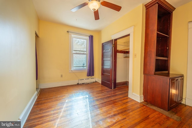 unfurnished bedroom featuring a spacious closet, baseboard heating, dark hardwood / wood-style floors, a closet, and ceiling fan