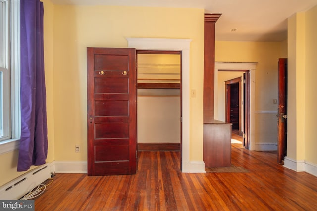 unfurnished bedroom with a baseboard heating unit and dark hardwood / wood-style floors