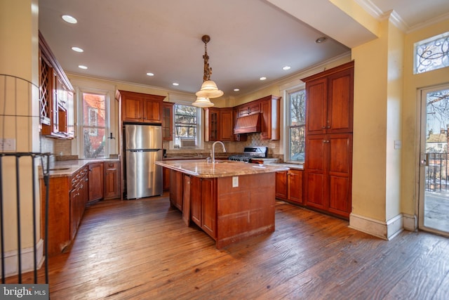 kitchen featuring pendant lighting, stainless steel refrigerator, an island with sink, ornamental molding, and light stone countertops