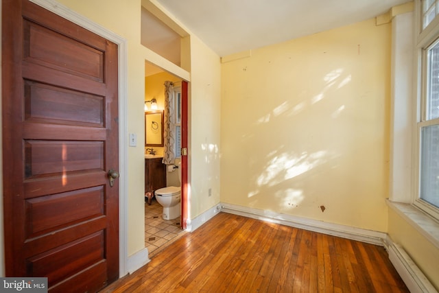 unfurnished bedroom with baseboard heating, connected bathroom, and dark hardwood / wood-style flooring