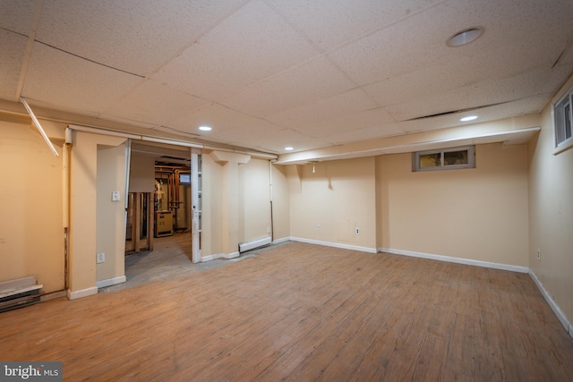 basement with a baseboard radiator, wood-type flooring, and a paneled ceiling