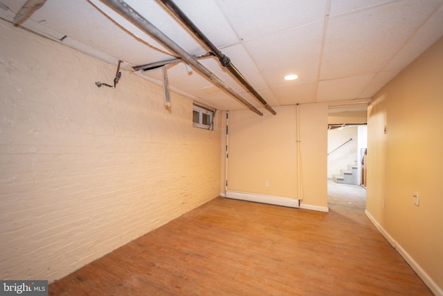 basement featuring hardwood / wood-style flooring, a baseboard radiator, and a drop ceiling