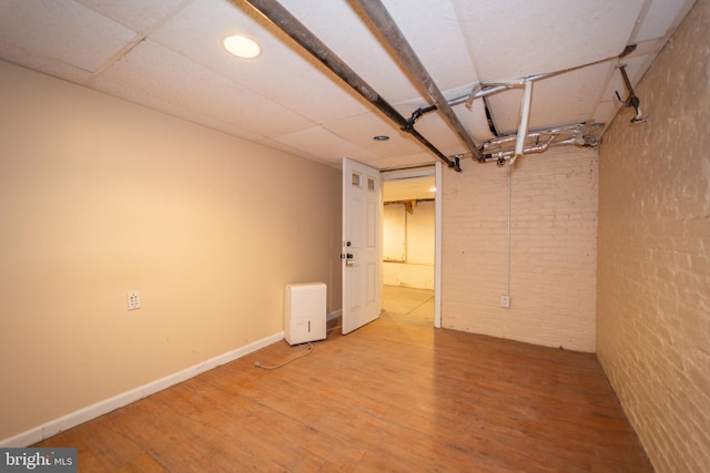 basement with a drop ceiling, wood-type flooring, and brick wall