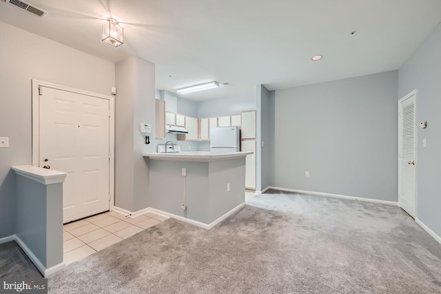 kitchen featuring white fridge, light colored carpet, kitchen peninsula, and white cabinetry