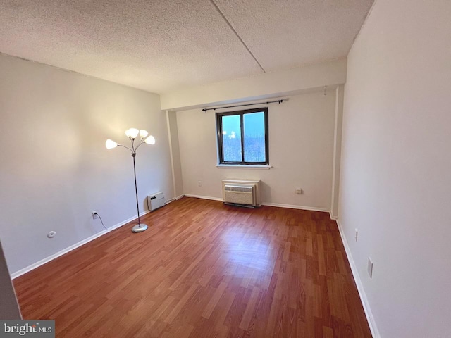 empty room with wood-type flooring, a textured ceiling, and a baseboard radiator