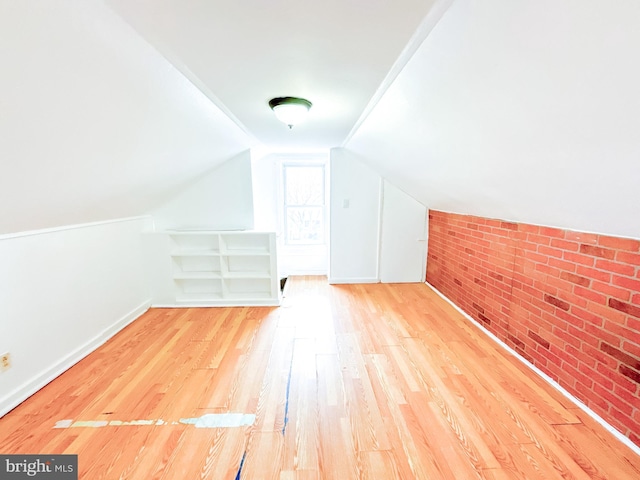 additional living space with wood-type flooring, lofted ceiling, and brick wall