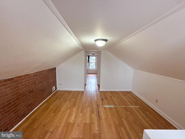 additional living space with light hardwood / wood-style flooring, brick wall, and lofted ceiling