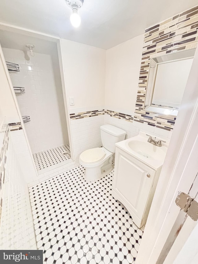 bathroom with a tile shower, tile patterned floors, toilet, vanity, and tile walls