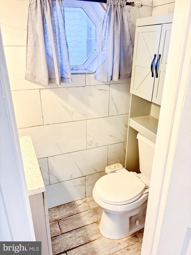 bathroom with toilet, wood-type flooring, and tile walls