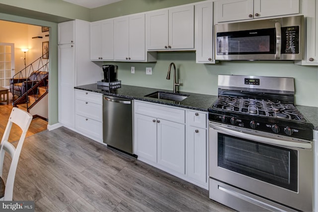 kitchen featuring appliances with stainless steel finishes, dark stone counters, sink, white cabinets, and light hardwood / wood-style floors