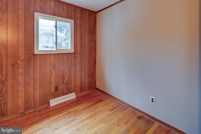 spare room featuring light hardwood / wood-style flooring, crown molding, and wood walls