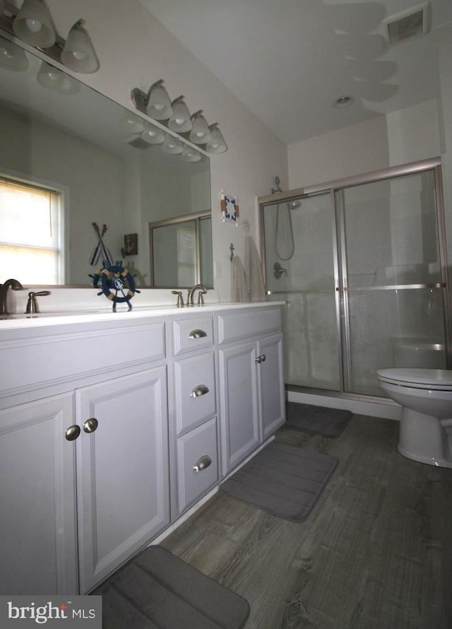 bathroom featuring a shower with door, vanity, wood-type flooring, and toilet