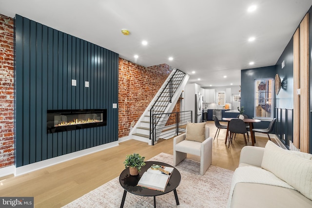 living room with a fireplace, light wood-type flooring, and brick wall