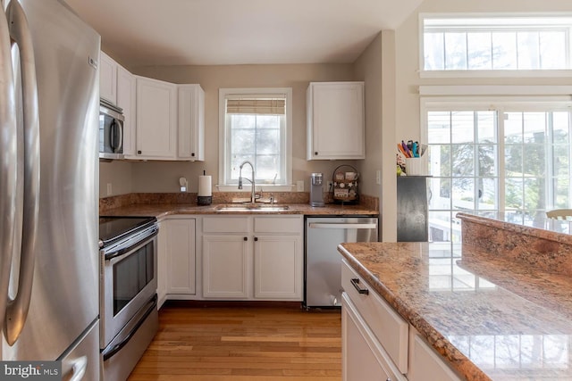 kitchen with a healthy amount of sunlight, white cabinets, sink, light hardwood / wood-style floors, and stainless steel appliances