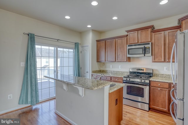 kitchen featuring a center island, a breakfast bar area, light hardwood / wood-style flooring, light stone counters, and stainless steel appliances