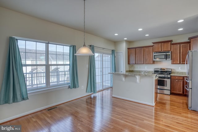 kitchen featuring plenty of natural light, stainless steel appliances, decorative light fixtures, and light hardwood / wood-style flooring