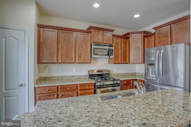 kitchen featuring stainless steel appliances, light stone counters, and sink