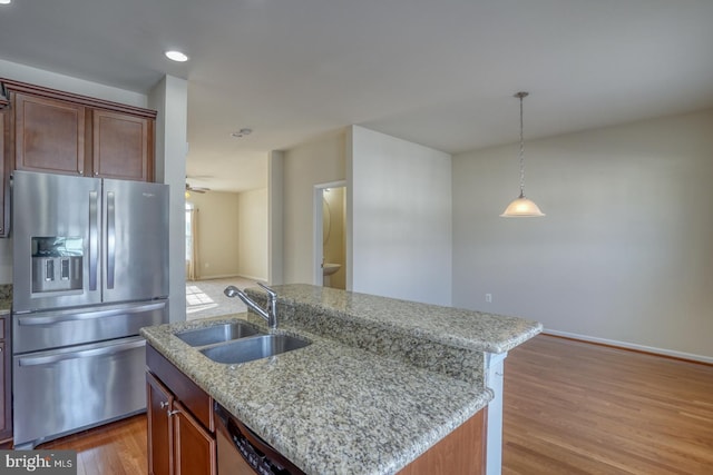 kitchen featuring light stone counters, stainless steel appliances, sink, hardwood / wood-style floors, and an island with sink