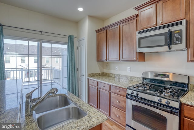 kitchen with light stone countertops, appliances with stainless steel finishes, light wood-type flooring, and sink