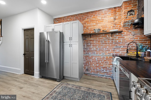 kitchen with sink, appliances with stainless steel finishes, light hardwood / wood-style floors, white cabinetry, and brick wall