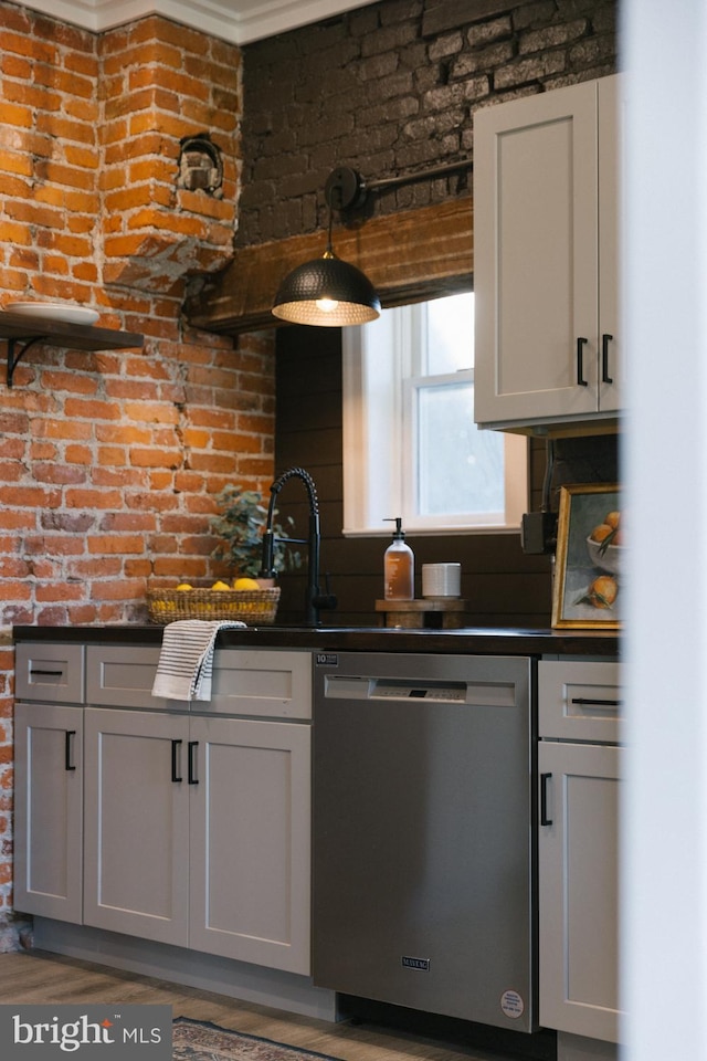 kitchen featuring gray cabinets, dark hardwood / wood-style floors, stainless steel dishwasher, and brick wall