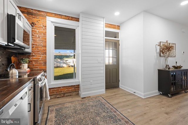 kitchen with white cabinets, stainless steel appliances, light hardwood / wood-style flooring, and brick wall