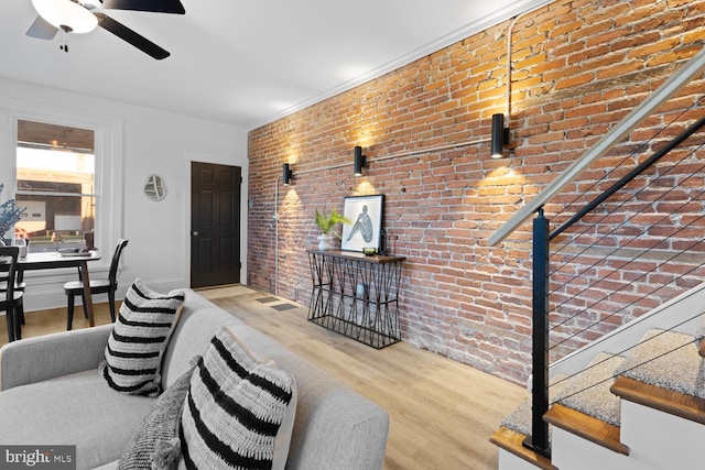 living room featuring hardwood / wood-style floors, ceiling fan, and brick wall